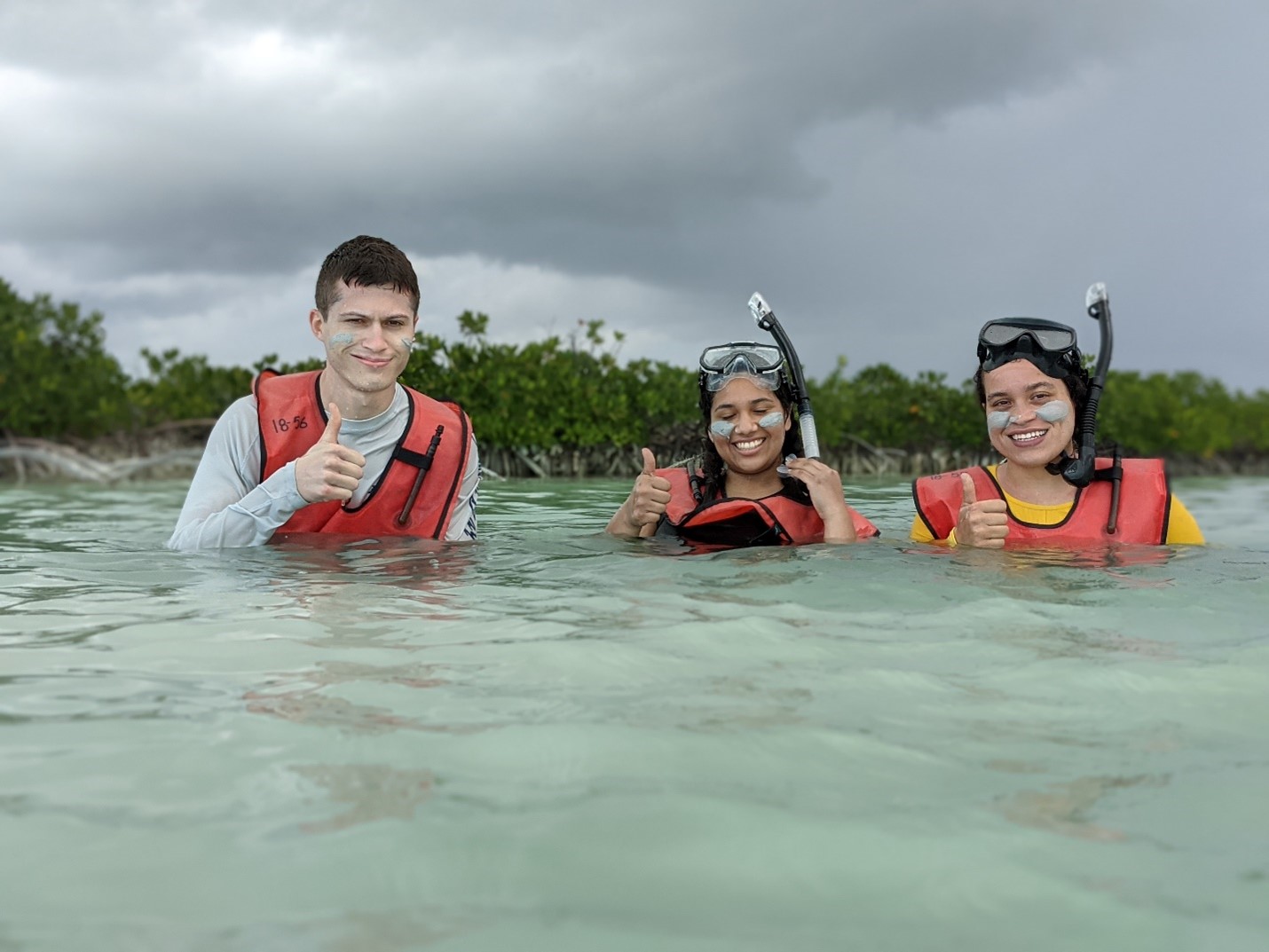 Geology undergraduate students (from left to right) Dennis Zakowicz, Barbara Reyes, and Bronte Heerdink snorkel in the tidal channel and paint their faces with carbonate mud.
