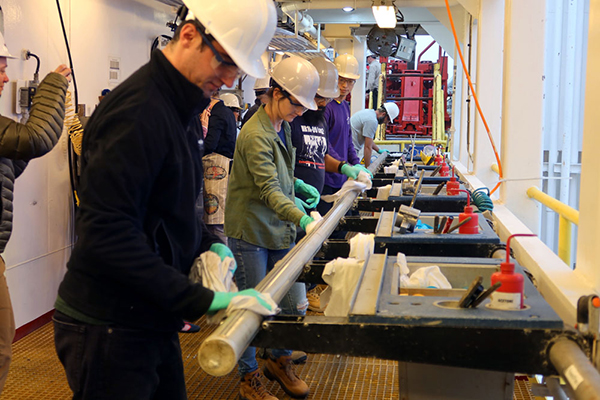 With the very first core of the expedition, Daniel Marone, IODP JRSO Electronics Specialist, Nicolette Lawler, IODP JRSO Marine Laboratory Specialist, and others. (Photo credit: Yiming Yu and IODP.)