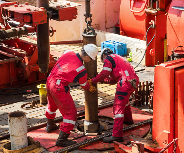 Siem Offshore personnel place the drill bit into position on the rig floor. (Photo credit: Tim Fulton, IODP JRSO.)