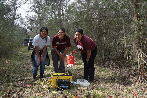 Three students in forest with geophysics equipment