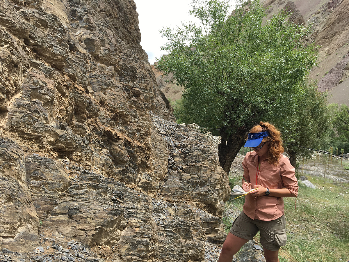 Melanie Bowen standing at an outcrop of the Himalayas, taking field notes.