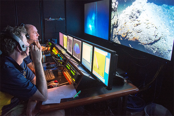 Scott Sofolofsky (background) and GISR PI Chip Breier (foreground) work in the ROV control room on the E/V Nautilus.