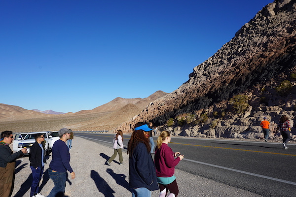 Students investigate a road cut outside of Death Valley National Park, CA. The road cut exposes a noticeable black geologic unit, obsidian volcanic glass, and the surrounding brown area, aka a baked zone, and the surrounding, unbaked, light gray sedimentary unit. (Photo courtesy of Dr. Brian Balta.)